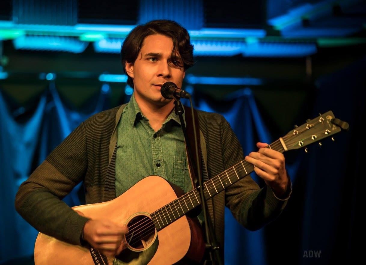 Jon Lewis singing and playing a guitar